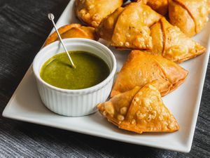 Samosas on a serving plate with a ramekin of herb chutney alongside