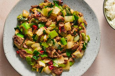 斑点陶瓷板控股美籍西班牙人的服务y stir-fried beef with leeks and onions. There is a small bowl of white rice in the top right corner of the image.