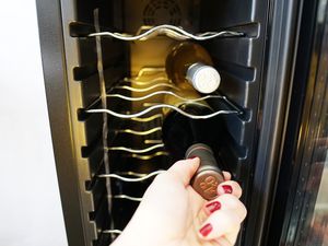 a hand removing a bottle of wine from a wine fridge