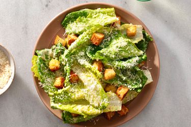 A composed caesar salad in a ceramic bowl on a white stone background.