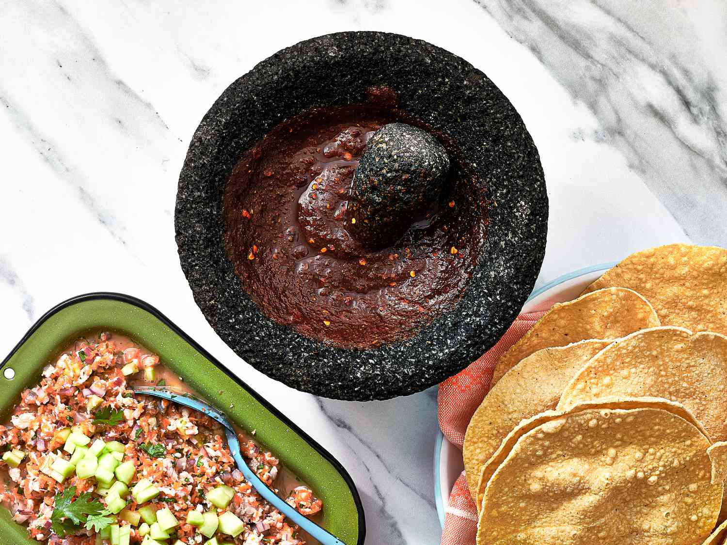 Overhead view of salsa negra in a molcajete with tostadas and ceviche