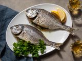 Two whole roasted daurade (orata) sit in a platter with some lemon wedges and parsley garnishing the plate