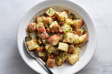 German potato salad in a white ceramic bowl with a spoon.