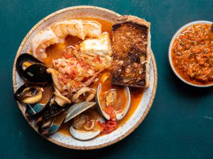 一份盛在碗里的cioppino，里面满是丰满的虾、贻贝、蛤蜊、鱿鱼、鱼等。旁边有一块深烤的酸面包，还有一个小碗，里面盛着烤红辣椒调味品。