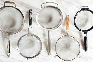 five fine mesh strainers on a marble countertop