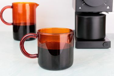 a Manual amber glass coffee mug next to a carafe and coffee grinder