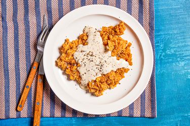 Chicken fried steak on a white plate on a purple and pink stripped towel on a blue backdrop