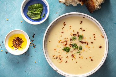 roasted garlic and parmesan soup in a bowl with red pepper flakes and basil as garnish