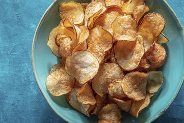 A blue ceramic bowl of potato chips on a blue background.