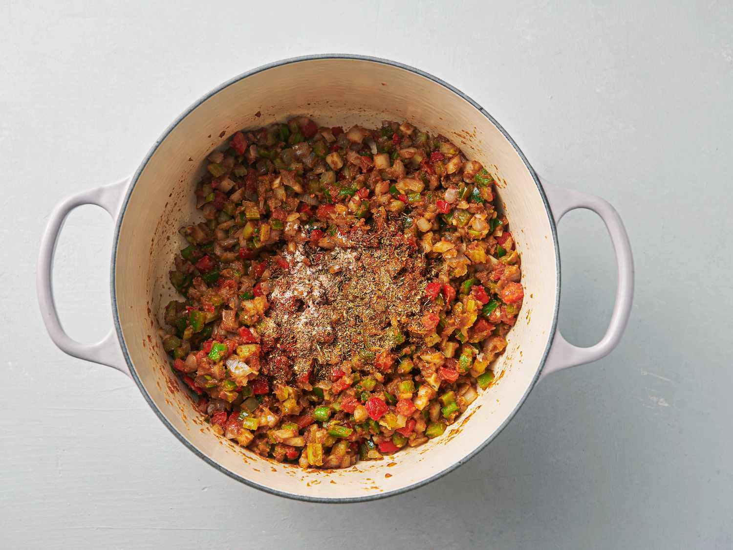 Dried oregano, dried thyme, garlic powder, onion powder, cayenne, and hot paprika stirred into vegetables inside Dutch oven