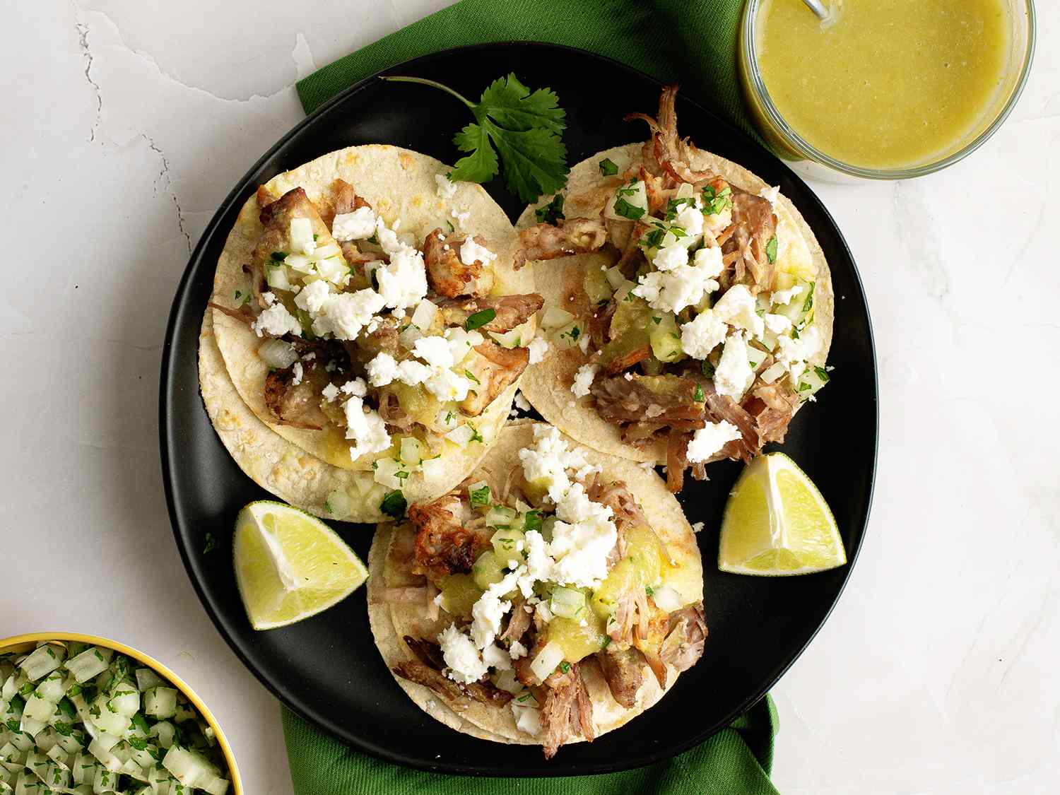 Plate of carnita tacos topped with salsa verde, onions, cilantro, and queso fresco.