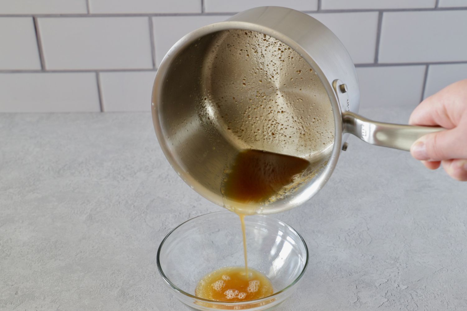 a small saucepan pouring browned butter into a small glass bowl.