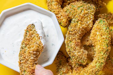 Overhead view of dipping an avocado fry into ranch on a yellow plate