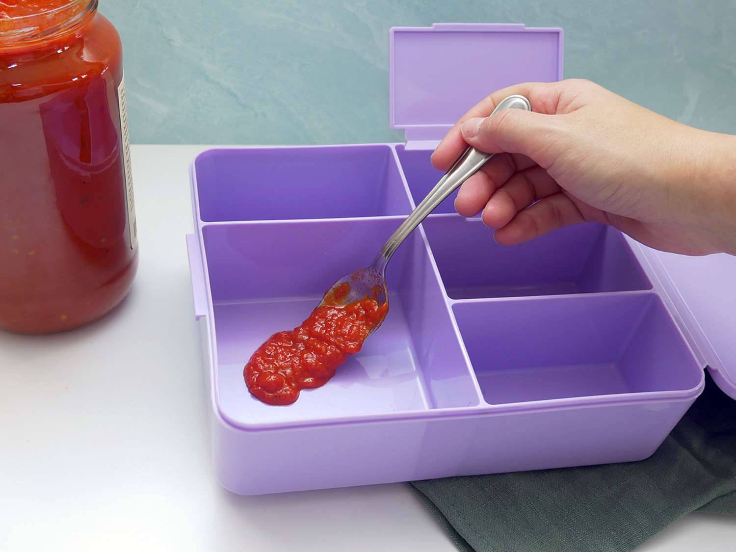 placing a spoonful of tomato sauce into the pottery barn bento box for the stain test.