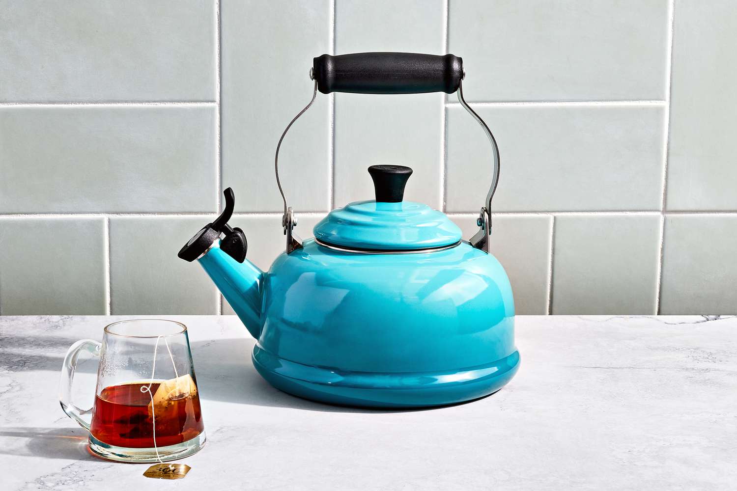 勒幅et Classic Whistling Kettle displayed on a marble countertop next to glass cup with tea inside