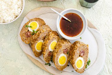 Embutido cut into 5 pieces and plated next to sauce and a serving of rice