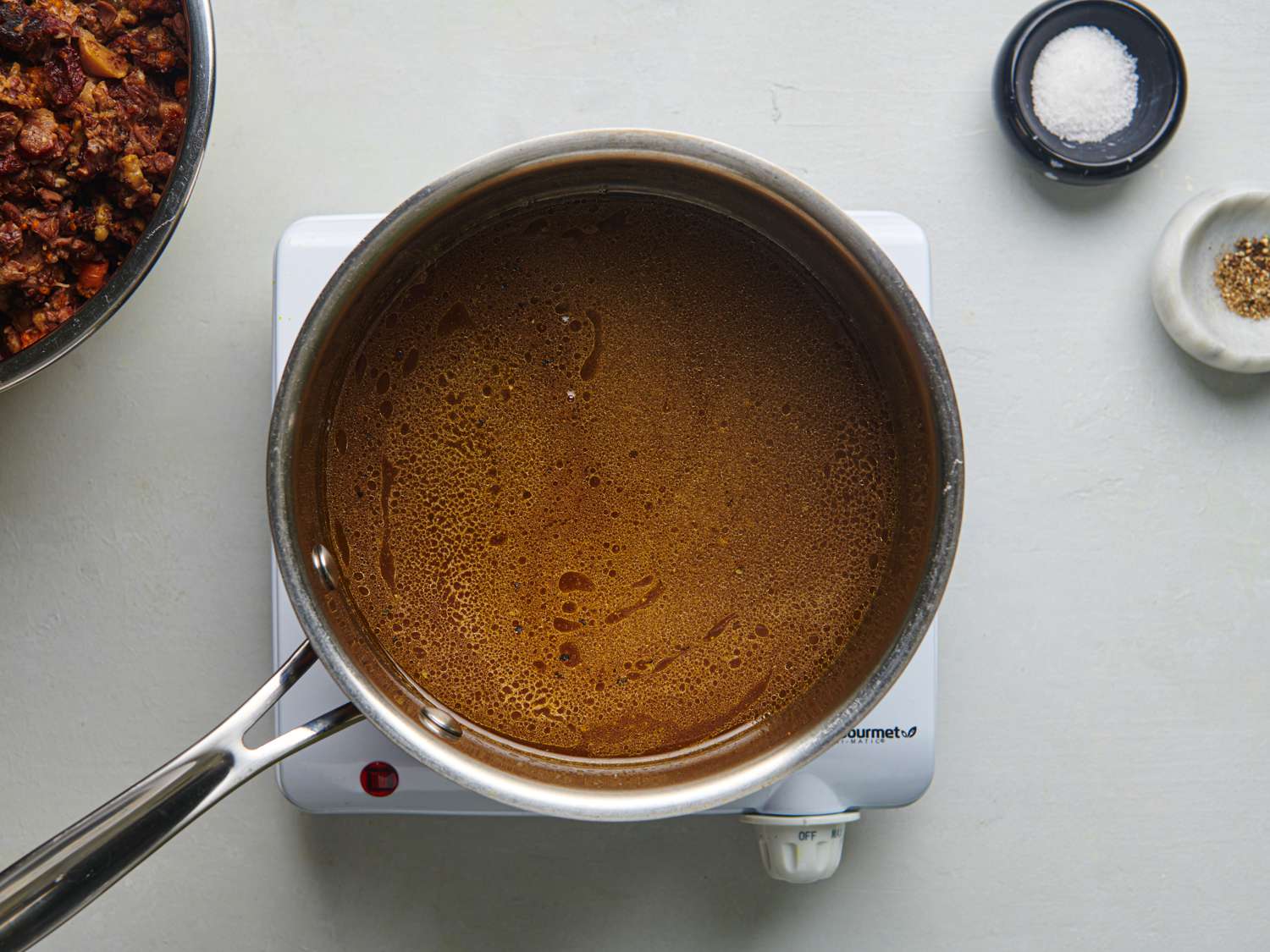 A medium-sized saucepan containing strained beef broth seasoned with salt and black pepper.