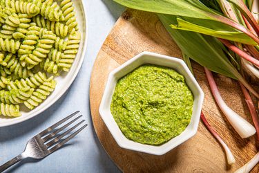 Overhead view of pesto in a small bowl next to ramps and pesto pasta