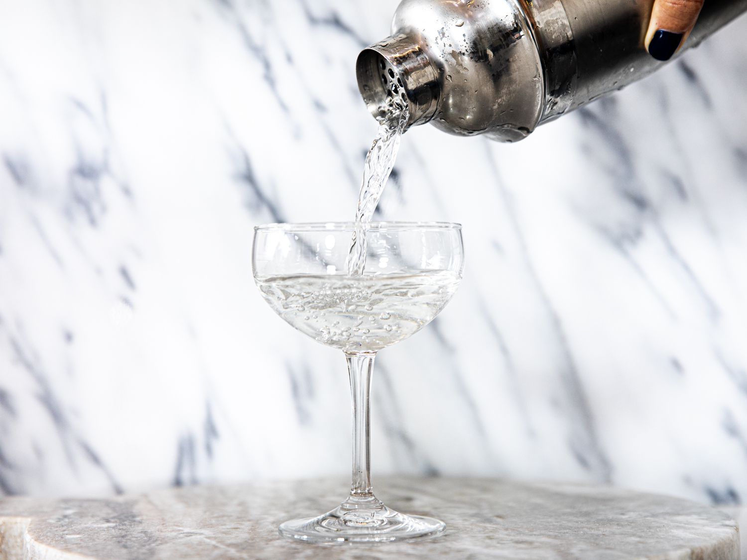 a cocktail being poured in a coupe glass from a cobbler shaker