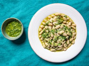 顶视图的大蒜柱身酱在一个小弓l next to a wide rimmed, shallow bowl of cooked white beans and pesto