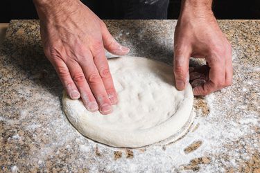 Hands shaping outdoor pizza oven pizza dough on a floured counter