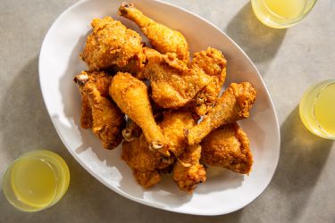 Platter of batter-fried chicken pieces flanked by yellow drinks on a marble countertop