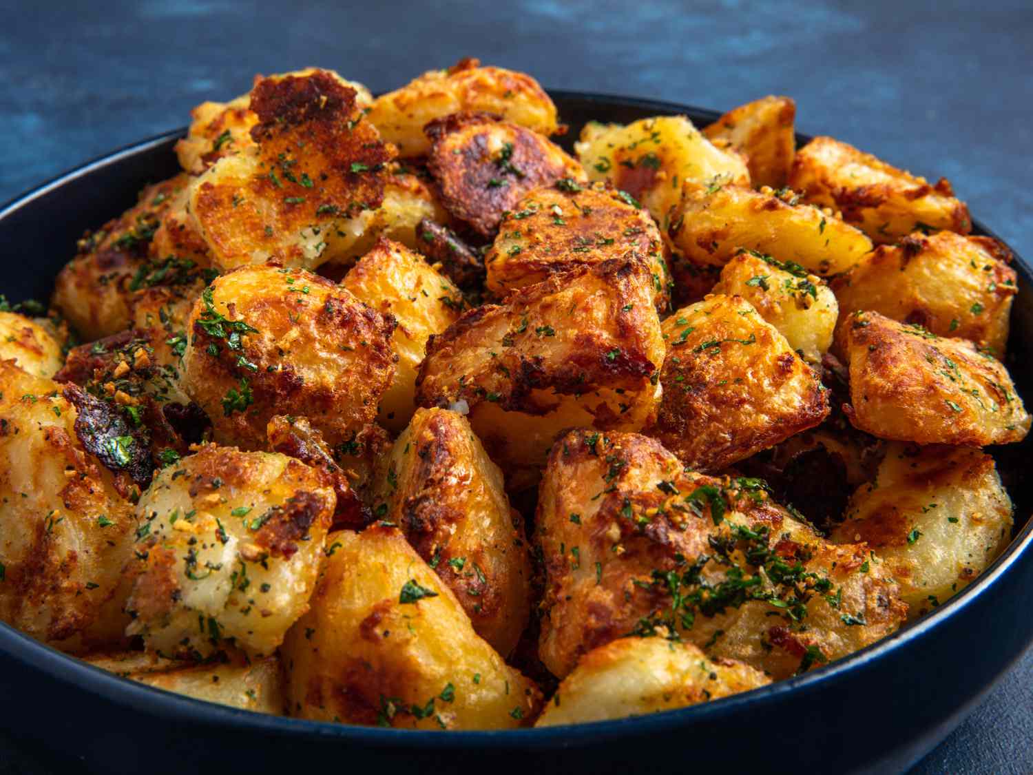 一个直角侧覆of the crispy roast potatoes in a bowl on a blue background.