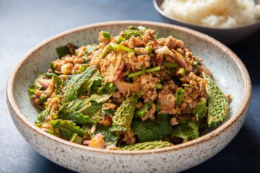 Serving bowl of pork laab with a bowl of sticky rice in the background