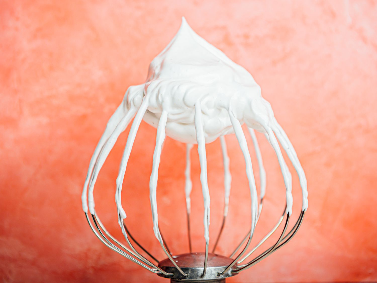 a whisk showing stiff white peaks with aquafaba meringue