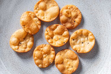 Golden brown chaat crisps resting on a ceramic plate.