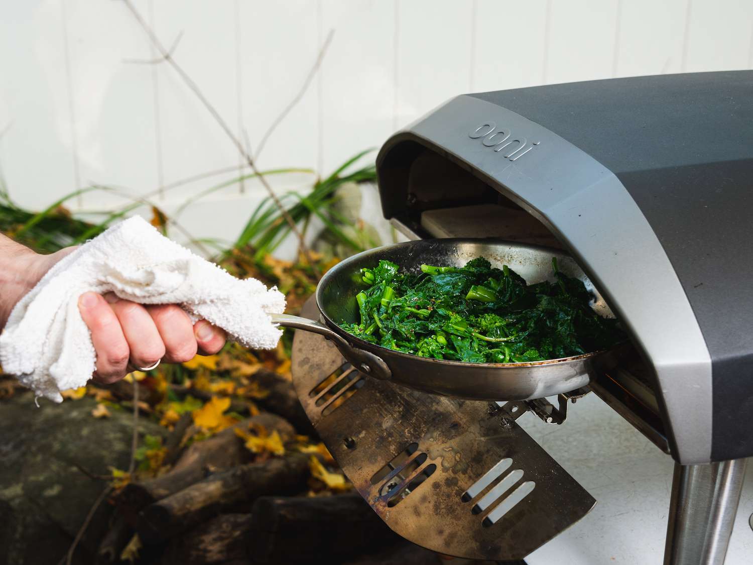 Charring broccoli rabe in a skillet in an outdoor pizza oven