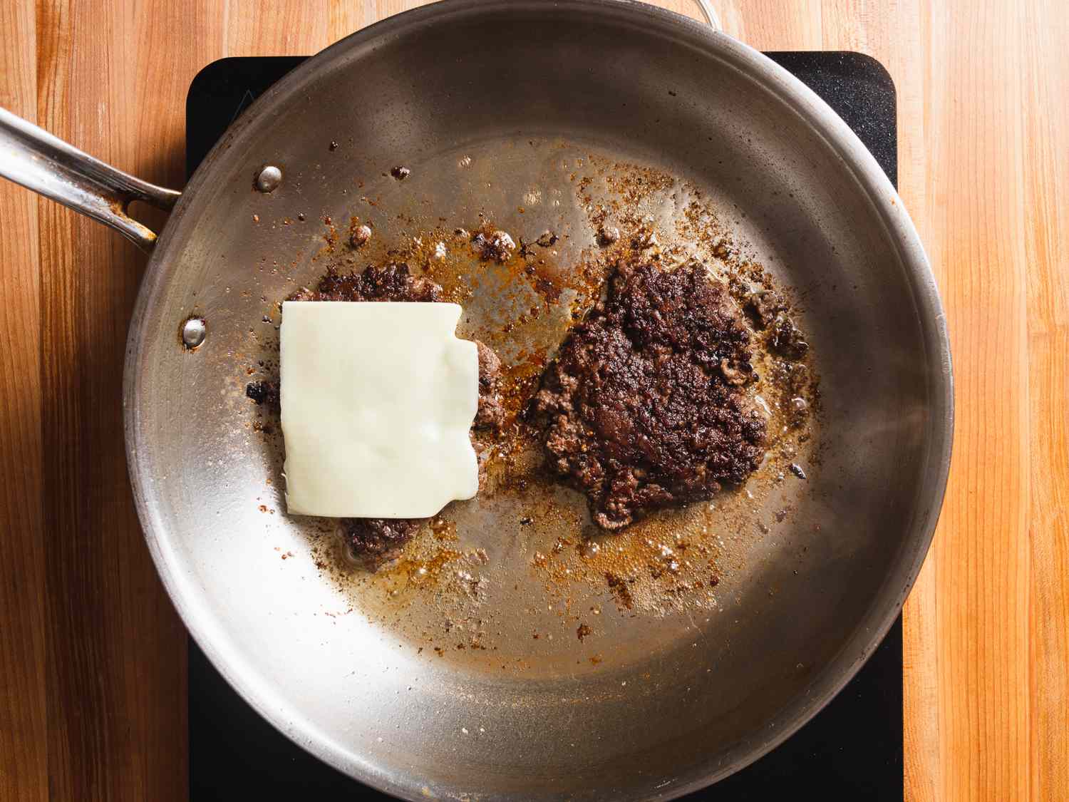 Smashed burgers in hot skillet after flipping, showing deep brown crust and adding cheese to one patty.