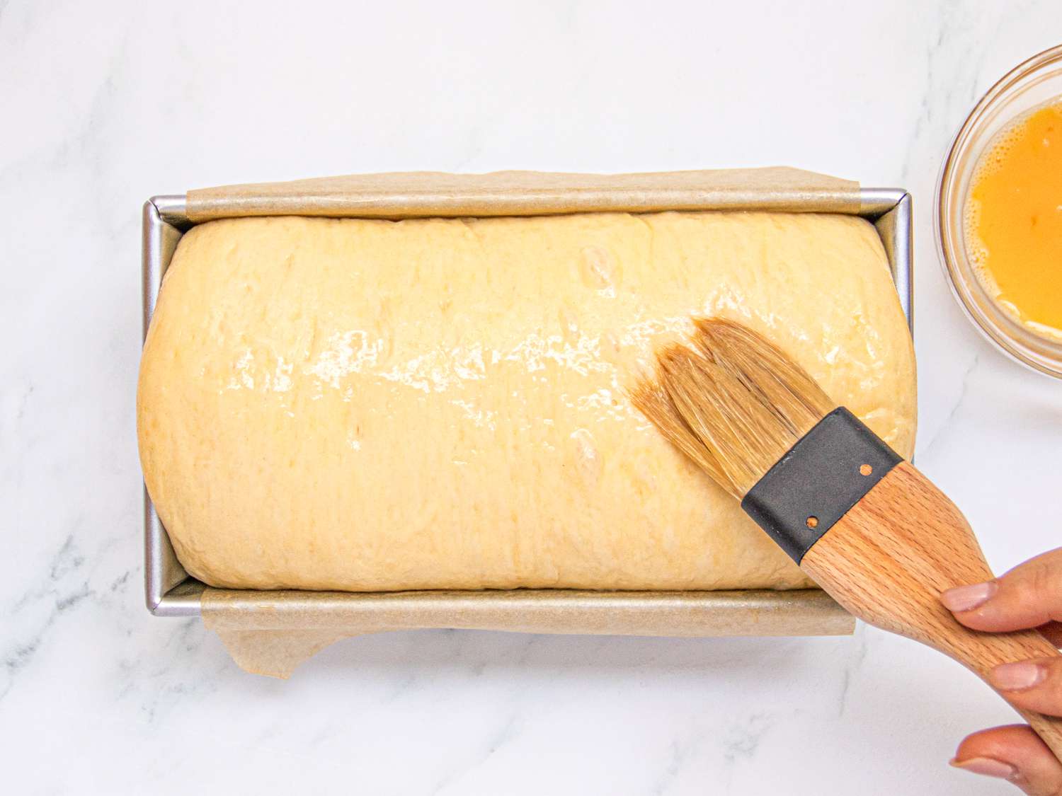 Overhead view of wiping brioche with egg wash