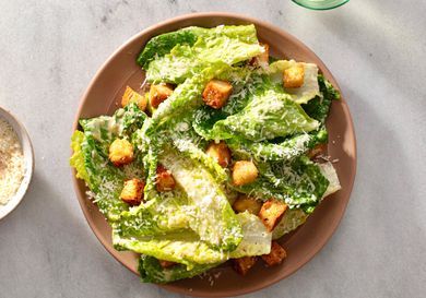 A composed caesar salad in a ceramic bowl on a white stone background.