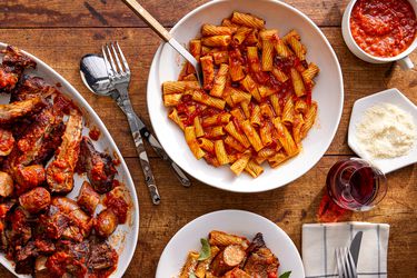 Overhead view of a tablescape of RagÃº Napoletano with pasta, a single serving, the platter of meat, extra sauce and extra cheese