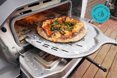 a pizza on a pizza peel coming out of a pizza oven