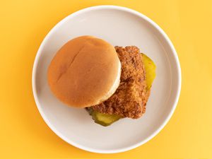 The fried chicken sandwich on a white plate on a yellow background.