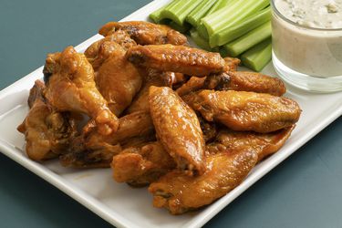 Oven-fried buffalo wings on a white rectangular plate with celery sticks and a glass cup of bleu cheese dressing.