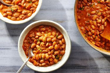 Two bowls and a pot of frijoles charros, on a stone background.