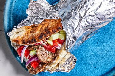 Greek-American Gryo wrapped in aluminum foil on a bright blue plate.