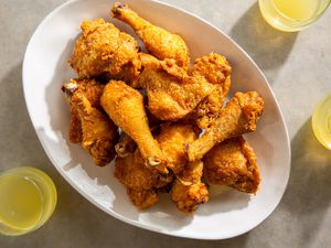 Platter of batter-fried chicken pieces flanked by yellow drinks on a marble countertop