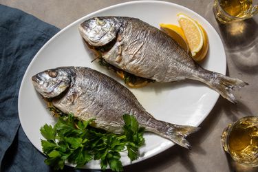 Two whole roasted daurade (orata) sit in a platter with some lemon wedges and parsley garnishing the plate