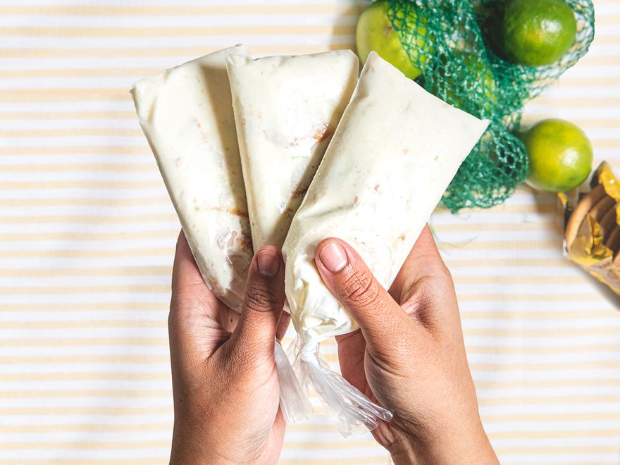 Overhead view of two hands holding three key lime bolis over a bag of limes and maria cookies