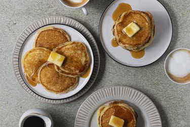 Plates of pancakes with butter and syrup on a stone counter.