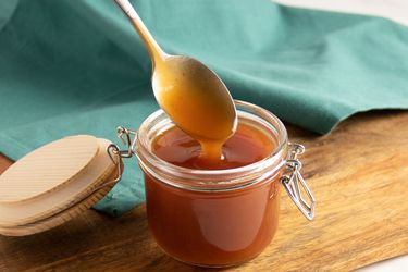 A spoon being pulled out of a glass jar of sweet and sour sauce.