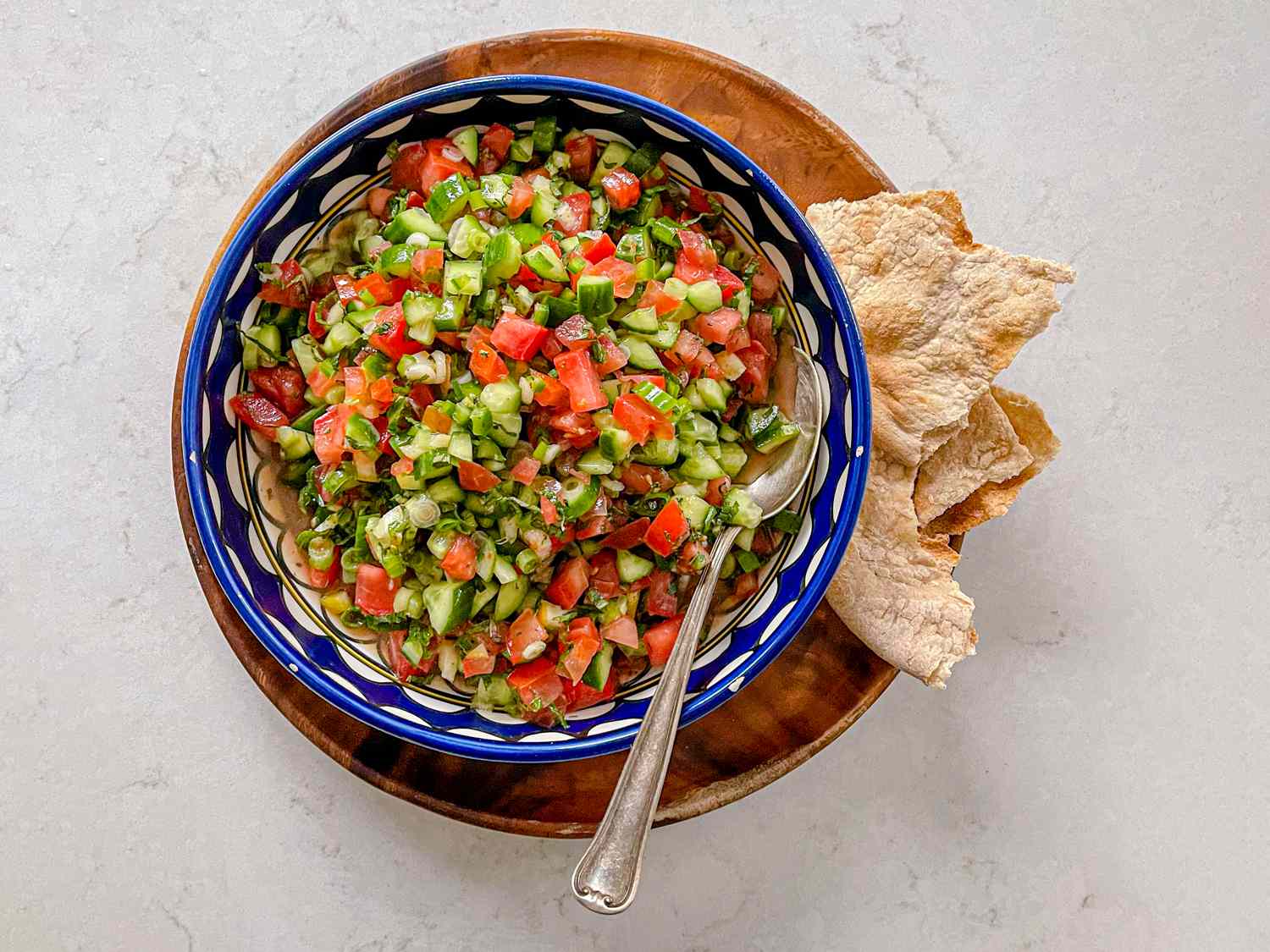 Overhead shot of Salata falahiyeh in a patterned blue bowl with crisp pita