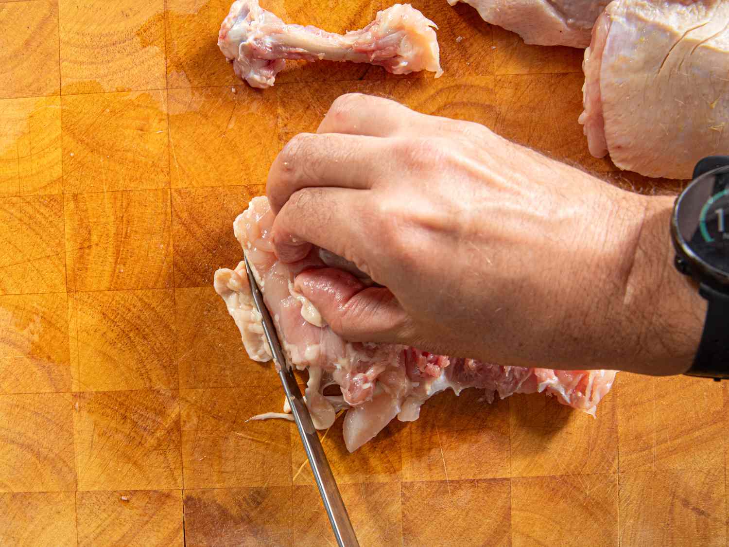 Overhead view of trimming fat off chicken thigh