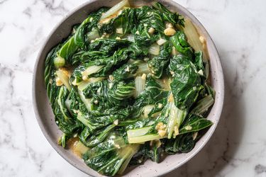 Stir fried choy sum and garlic on a ceramic plate on a stone background.