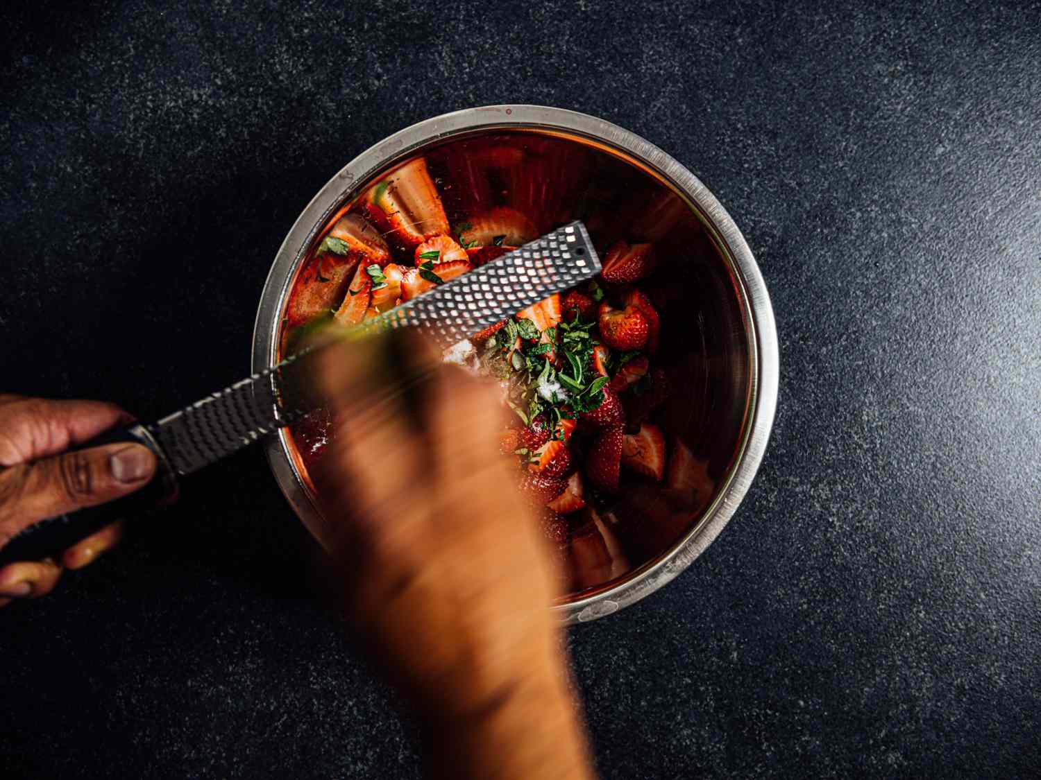 hands grating lime zest directly over strawberry mixture with a microplane