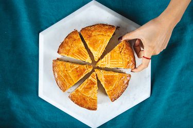 Overhead view of a sliced gateau basque cake with a hand reaching in for a slice